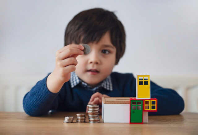 Blurry face of preschool kid showing 10 pence with smiling face, Selective focus kid boy making stack money coins and counting before puting in money box. Learning financial responsibility and planning