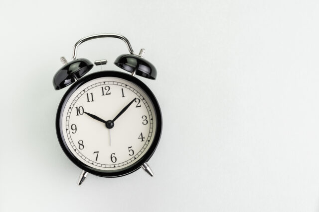 Flat lay of black alarm clock on texture white background with copy space using as time, deadline or schedule presentation wallpaper.